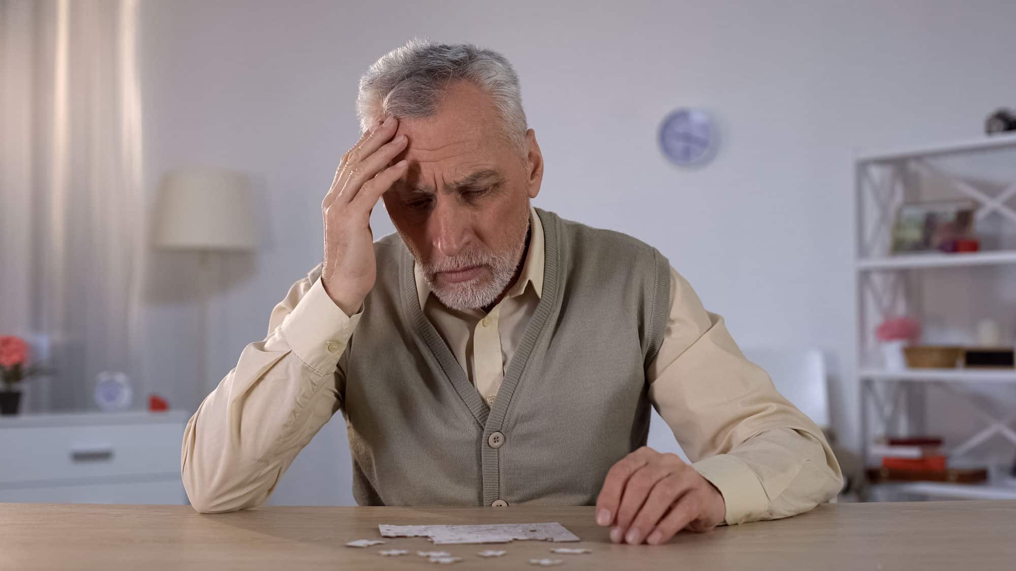 a senior man places hand to head while doing puzzle
