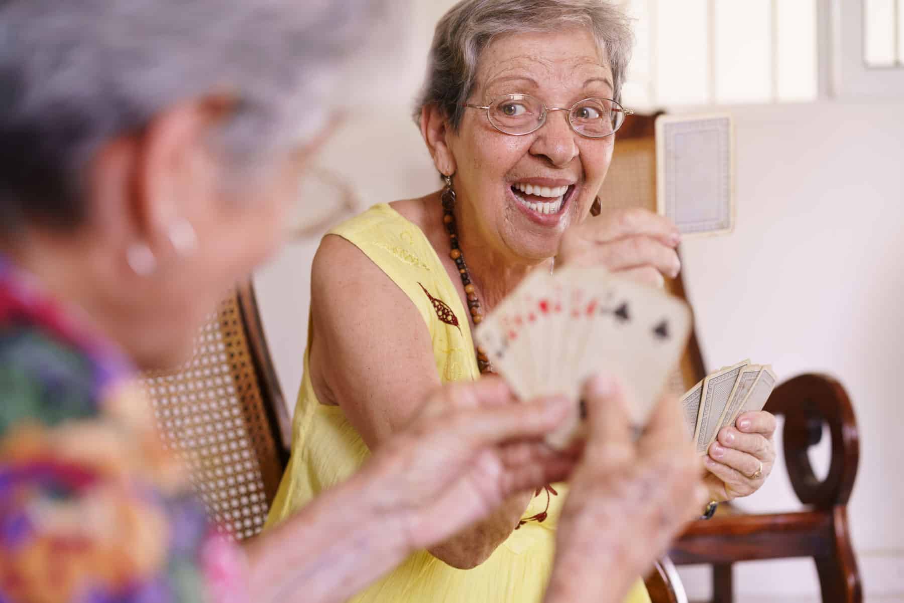 Two senior women laugh as they play cards