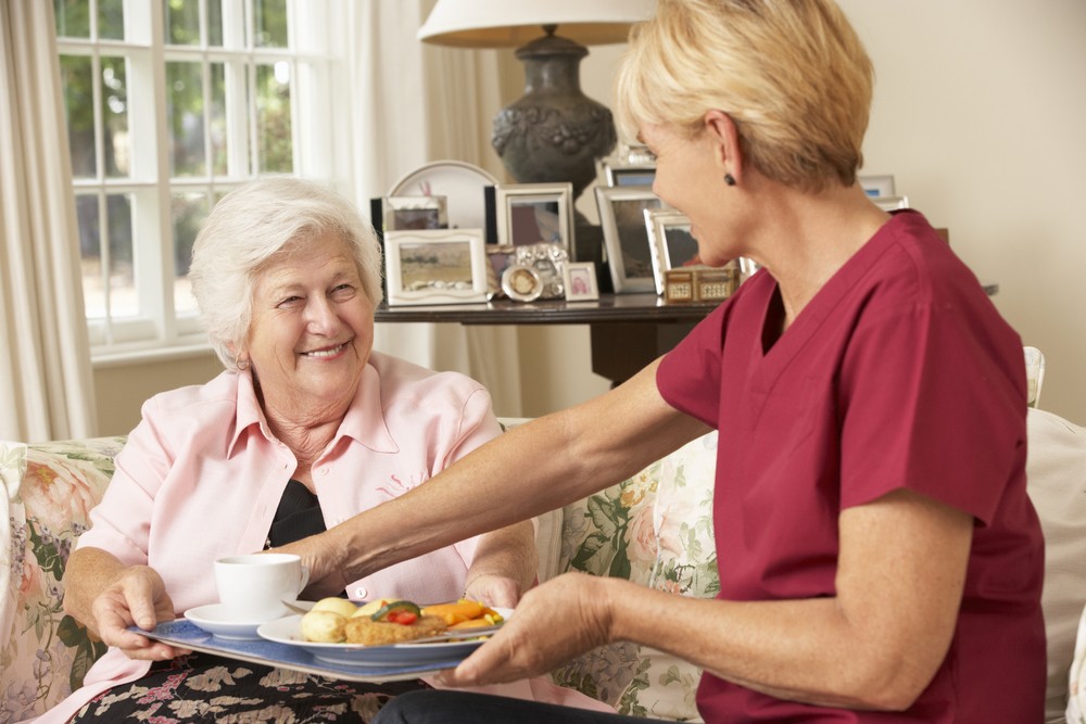 A nurse hands a tray of food to a senior women.