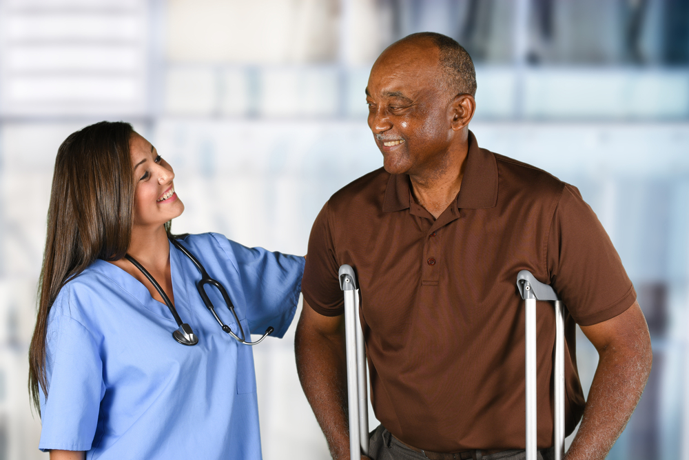 A senior man uses crutches to walk next to a nurse.